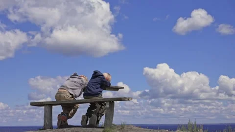 Two boys sitting on a bench enjoying the coastal view Stock Footage 338383901