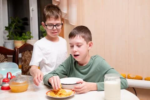 Two boys sitting at the kitchen table and picking up crunchy cornflakes Stock Photos