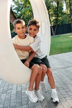 Two boys sitting on a round swing in a park during the day Stock Photos