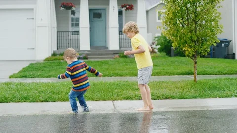 Two boys splash in the gutter outside their house on rainy afternoon slow motion Stock-Footage 127546095