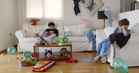 Two boys surrounded by toys in a cluttered living room during daytime play Stock Footage 274840229