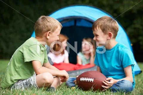 Two Boys Talking And Playing With American Football On Camping T Stock Photos