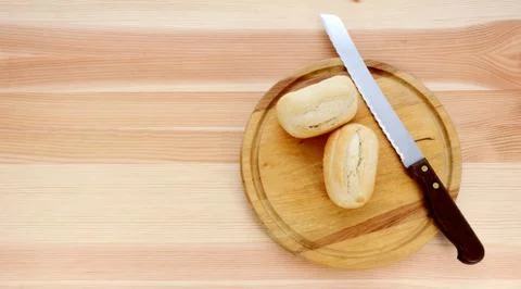 Two bread rolls, a knife and wooden cutting board Stock Photos