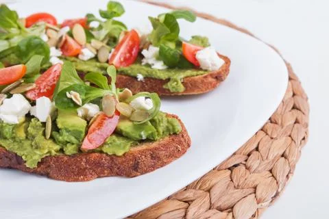Two bread toasts with mashed avocado, tomatoes and feta cheese. Stock Photos