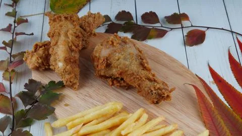 Two breaded chicken wings, one chicken leg and a bunch of golden french fries Stock Photos