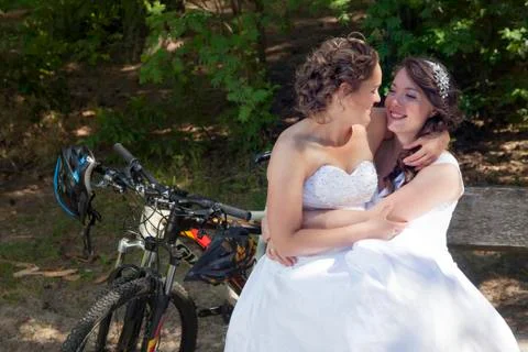 Two brides on bench in forest with mountain bikes Stock Photos
