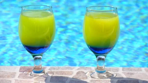 Two bright beautiful yellow-blue cocktails stand close-up on side pool Vidéo 132647802