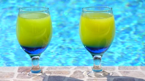 Two bright beautiful yellow-blue cocktails stand close-up on side pool Stock Footage 132648161