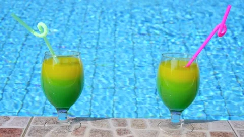Two bright beautiful yellow-green-orange cocktails with straws glasses stand Vidéo 130534825