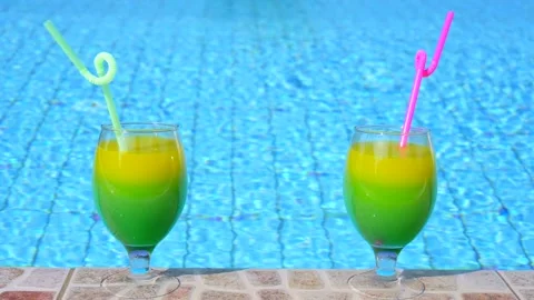Two bright beautiful yellow-green-orange cocktails with straws glasses stand Stock Footage 130570432