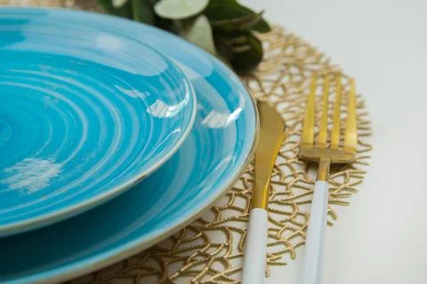 Two bright blue serving plates stand on a golden napkin, a fork of gold and Stock Photos