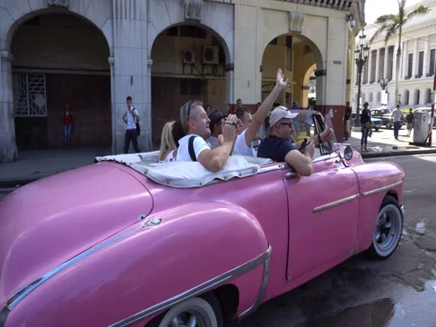 Two bright pink and orange retro car cabriolet leave the parking lot on a Stock Footage 71038154
