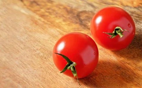 Two bright red cherry tomatoes on wooden board, space for text left side Foto stock