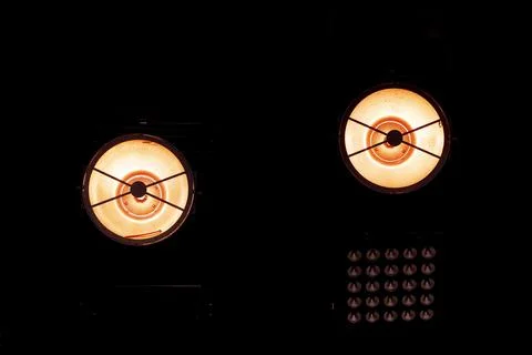 Two bright stage lights casting warm orange glow against a dark background Stock Photos