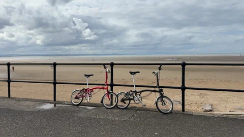 Two Brompton folding bikes leaning against a railing on Crosby Beach. Vidéo 316471899