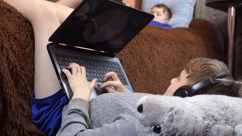 Two brothers are lying on the bed and playing on the laptop. Stock Footage 99045585