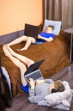 Two brothers are lying on the bed and playing on the laptop. Stock Photos