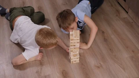Two brothers are playing a game with wooden blocks lying on the floor at home. Stock Footage 329276641