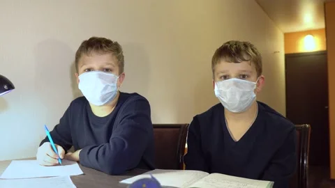 Two brothers are sitting in protective masks at home and doing their homework. T Stock Footage 130661332