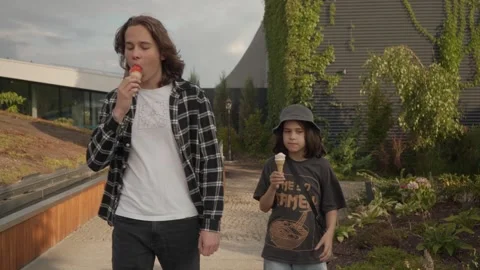 Two brothers are walking together in a city park and eating ice cream. Stock Footage 299544958