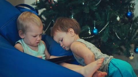 Two brothers of the boy play on a tablet (watch cartoons) on Christmas day Stock Footage 83723003