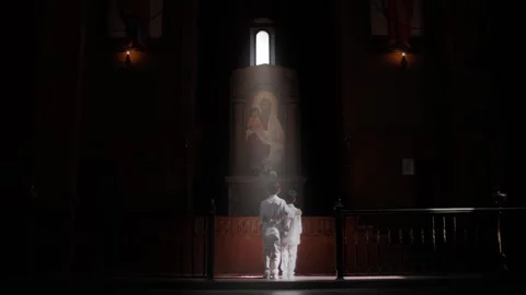 Two brothers come to stand in front of the cross in the church and light falls Stock Footage 232044404