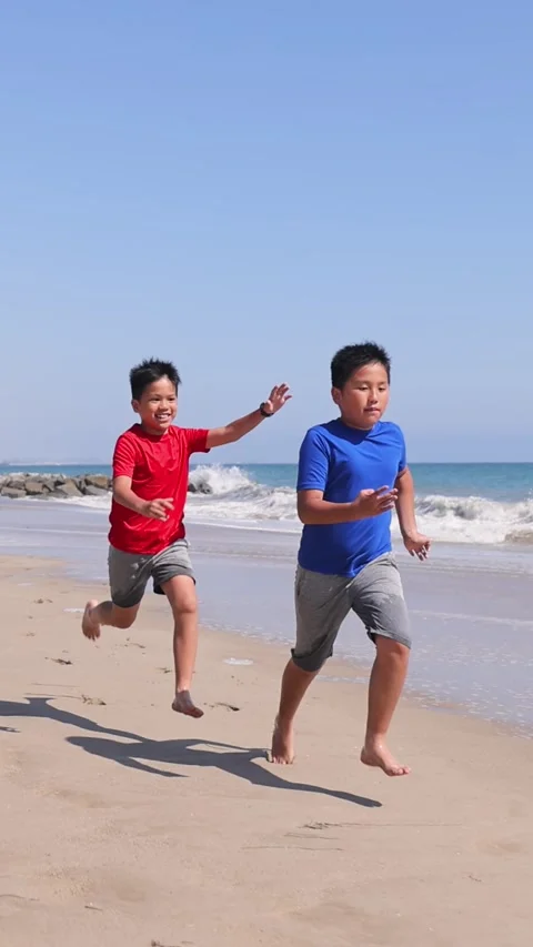 Two brothers playing tag on the beach. Vertical video. Stock Footage 337435528