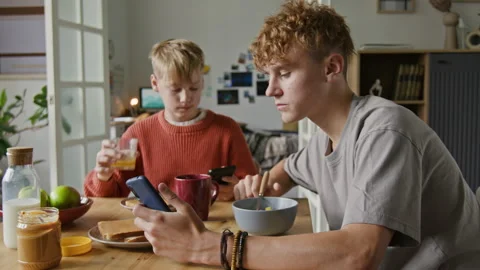 Two Brothers using Phones at Kitchen Table Eating Breakfast Stock Footage 318554587