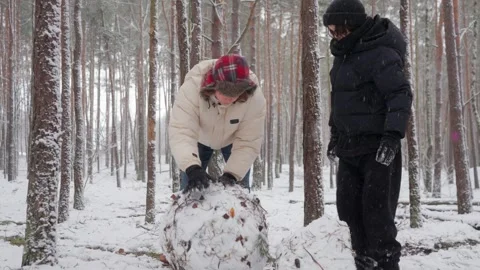 Two brothers work shoulder to shoulder rolling a giant snowball in the forest Stock Footage 312001007