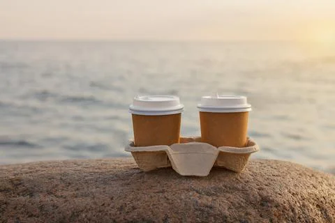Two brown cup of drink on stone by the sunset sea Stock Photos