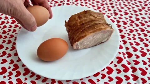 Two Brown Eggs and Cooked Meat on White Plate with Red Heart Tablecloth Stock Footage 333894607