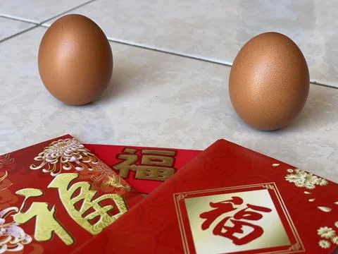 Two Brown Eggs Balancing Upright Near Red Envelopes For Lichun Foto stock