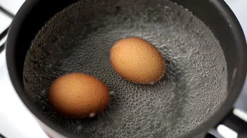 Two brown eggs in a pot of water at the beginning of the boil with bubbles Stock Footage 179921517