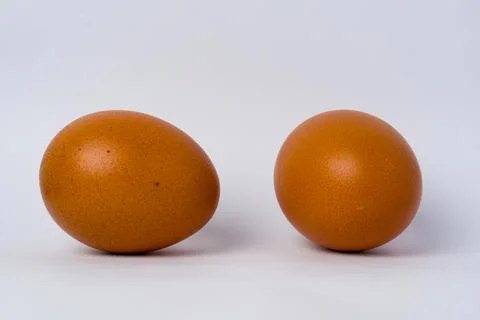 Two brown eggs sit side by side on a plain white surface Stock Photos