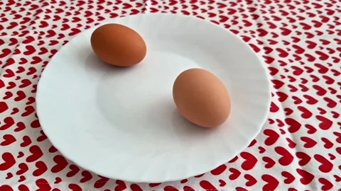 Two Brown Eggs on White Plate with Red Heart Pattern Tablecloth Background Stock Footage 333894554