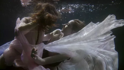 Two brunettes look at each other and float in the dark under the water. close-up Stock Footage 208379204
