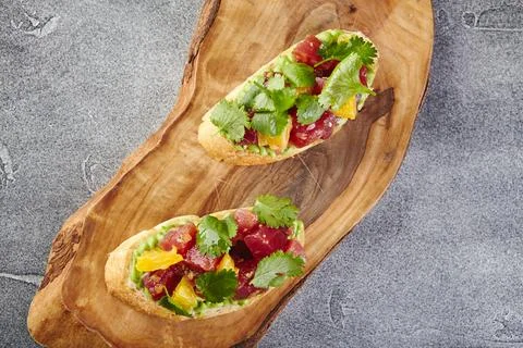 Two Bruschettas with Avocado paste, Tuna, Orange and cilantro on wooden cutti Stock Photos