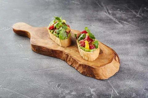 Two Bruschettas with Avocado paste, Tuna, Orange and cilantro on wooden cut.. Stock Photos