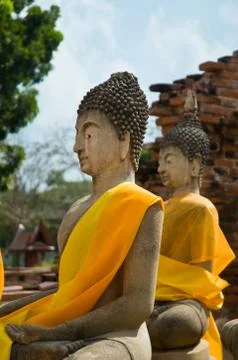 Two buddha statues wrapped in an orange scarf in a ancient surounding. Stock Photos