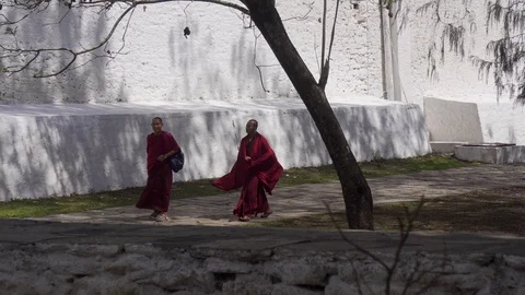 Two Buddhist monks walking fast around an ancient temple in Bhutan Stock Footage 105055661