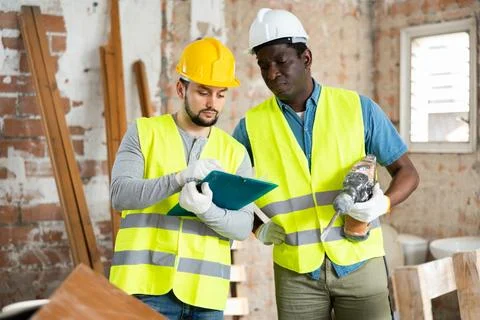 Two builders in with a hammer drill discuss work issues, making notes Stock Photos