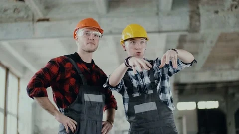 Two builders in helmets and overalls at a construction site assess the scope of Stock Footage 130776245
