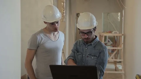 Two builders in helmets are typing a laptop and looking around. Stock Footage 77552763