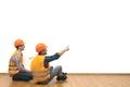 The two builders with a paper sit on the floor on the white wall background Photo