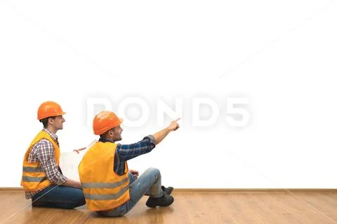 The two builders with a paper sit on the floor on the white wall background Stock Photos