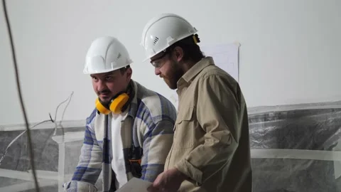 Two builders in white helmets discuss drawings on the construction site. Stock Footage 236762070