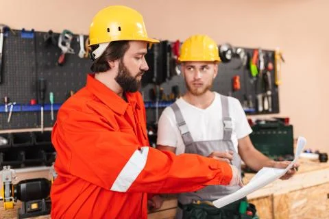 Two builders in work clothes and hardhats working in workshop wi Foto stock