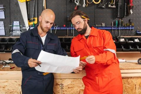 Two builders in work clothes thoughtfully looking on sketch with Stock Photos