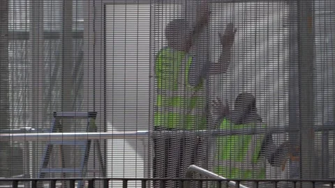 Two builders working on a wall behind a metal grid Vídeo Stock 250006747