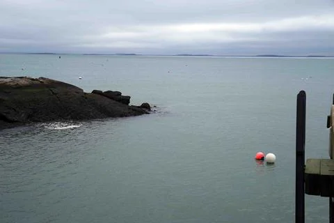 Two buoys float together by a dock along a rocky New England coastline Stock Photos